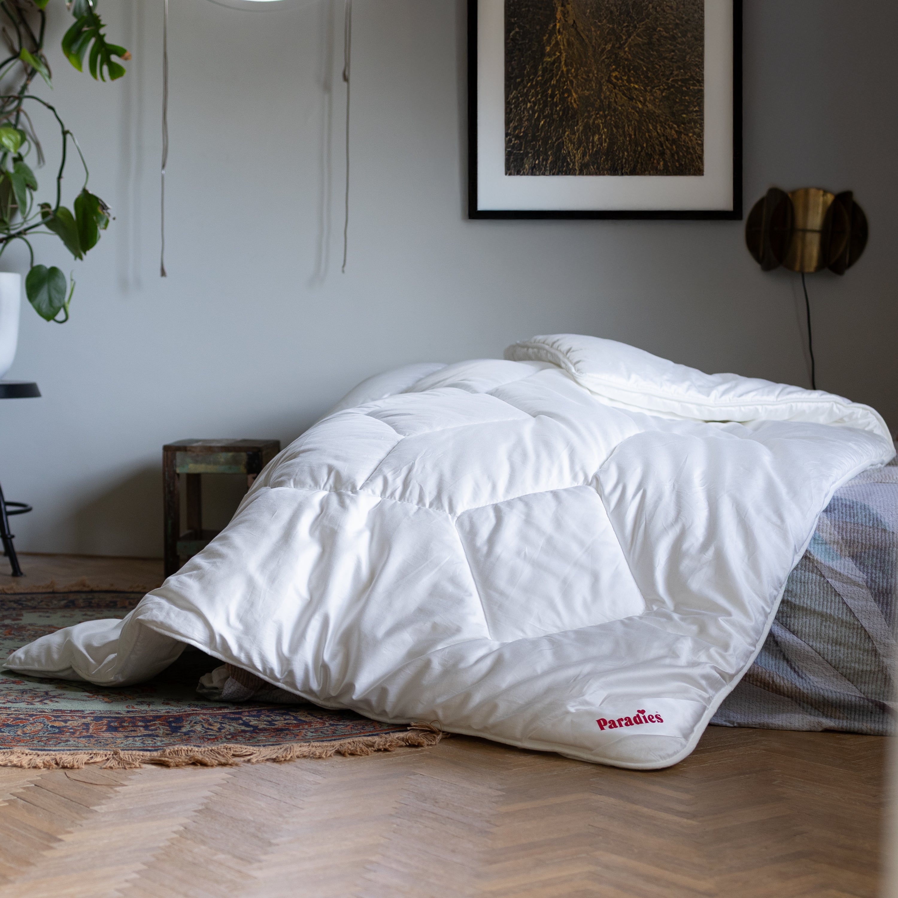 Weiße Prima Steppdecke liegt auf Bett in modernem Schlafzimmer mit Pflanzen und reicht bis auf den Holzfußboden.