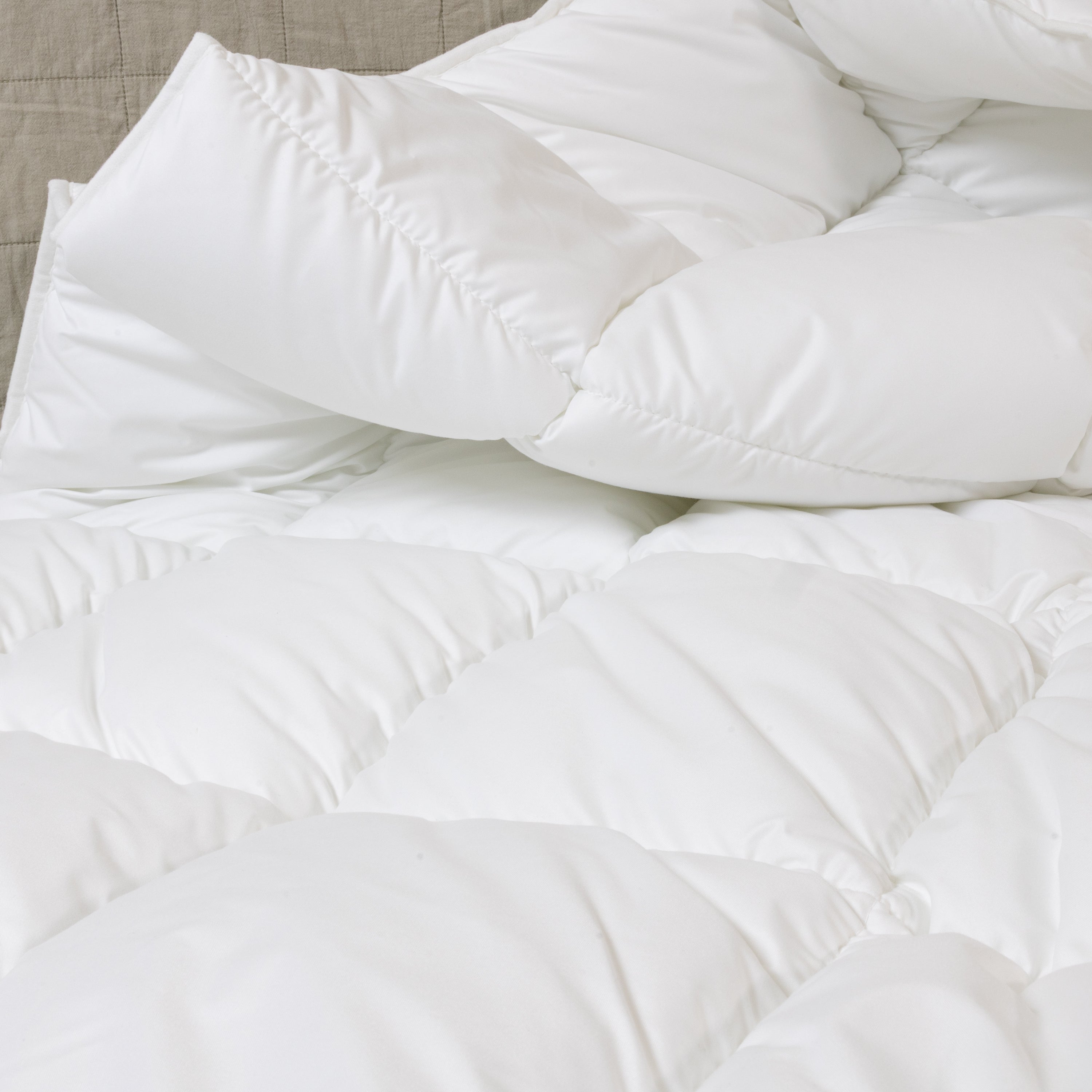 Bett mit weißer Steppdecke, mehreren weißen und einem rosafarbenen Kissen mit roter Aufschrift sowie einem Blumenstrauß in Vase auf Nachttisch