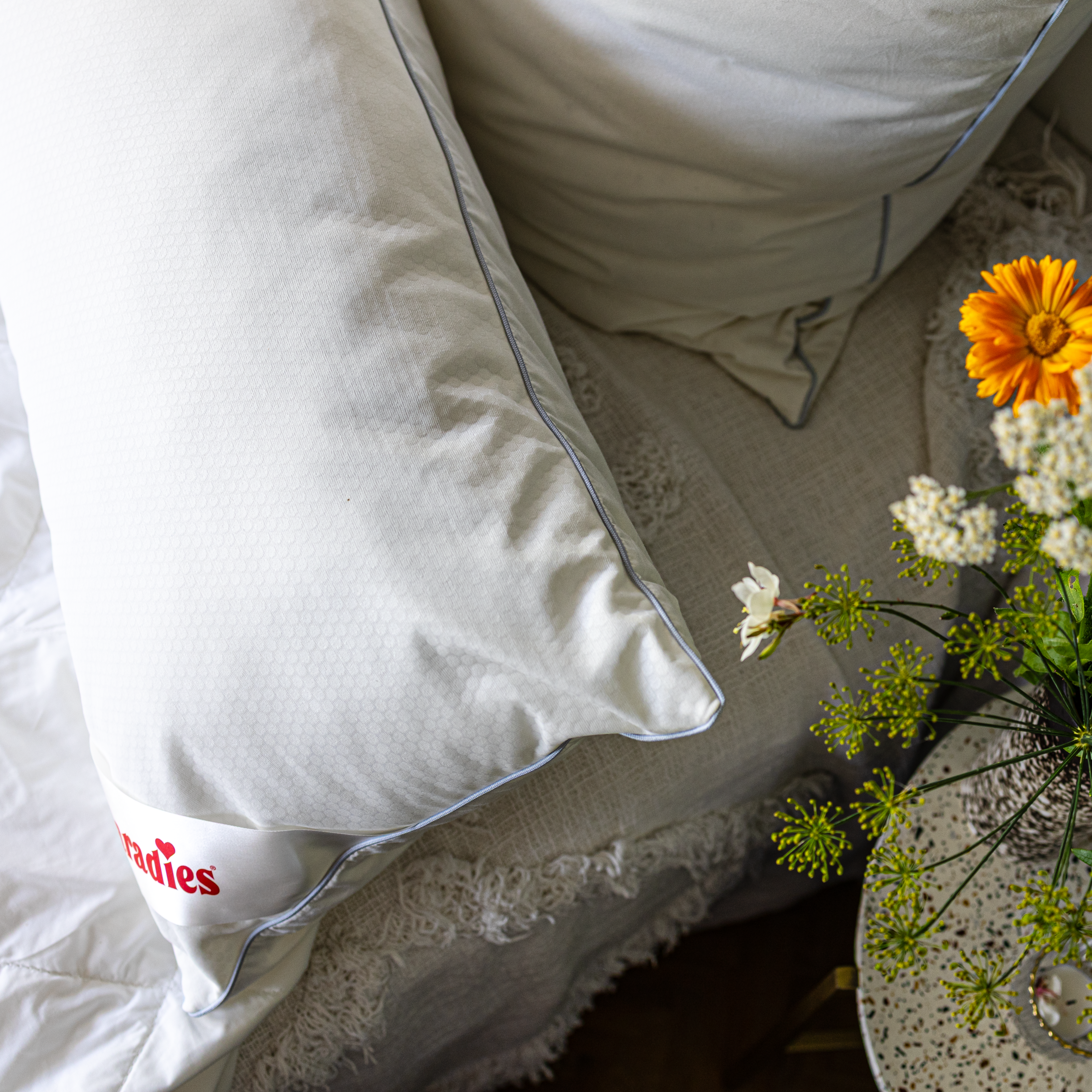 Paradies Softy Cool Dream Kissen auf einer hellen Decke neben einem Tisch mit bunten Blumen