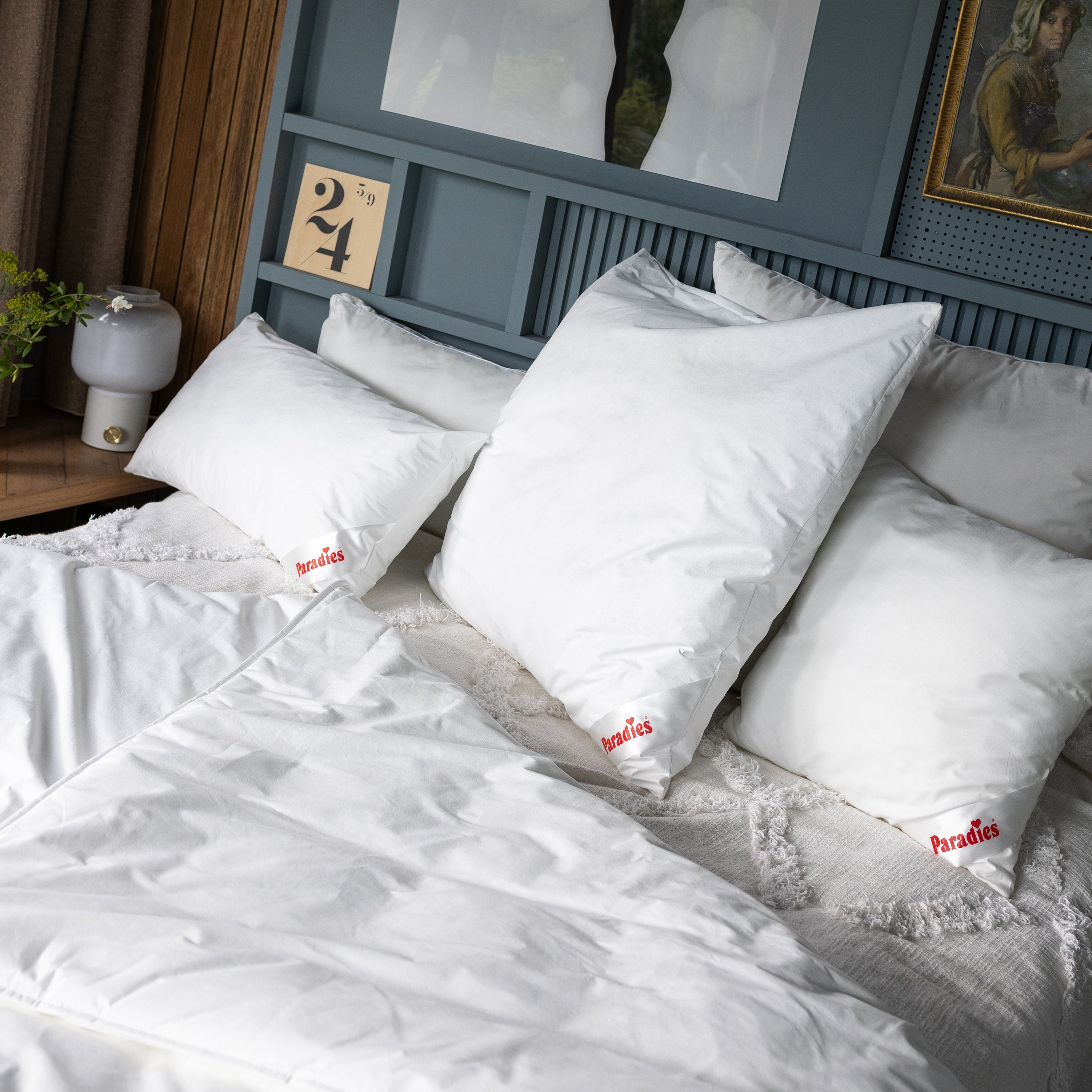 Drei weiße Softy Antiallergo Kissen mit rotem Paradies-Logo auf einem Bett mit Antiallergo Bettdecke und blauem Kopfteil