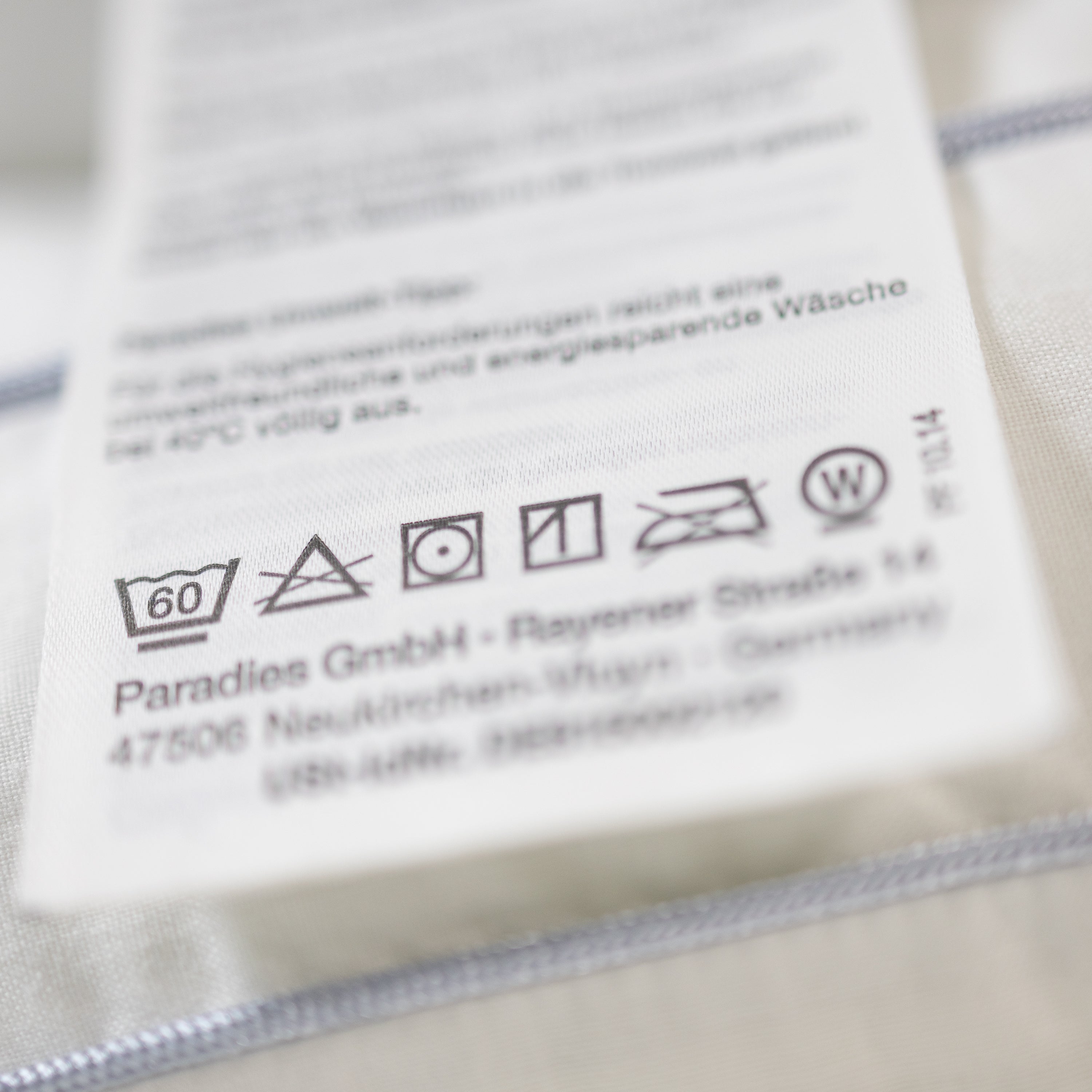 Pflegehinweise auf einem weißen Textil-Etikett mit Waschsymbolen und Herstellerangaben von Paradies