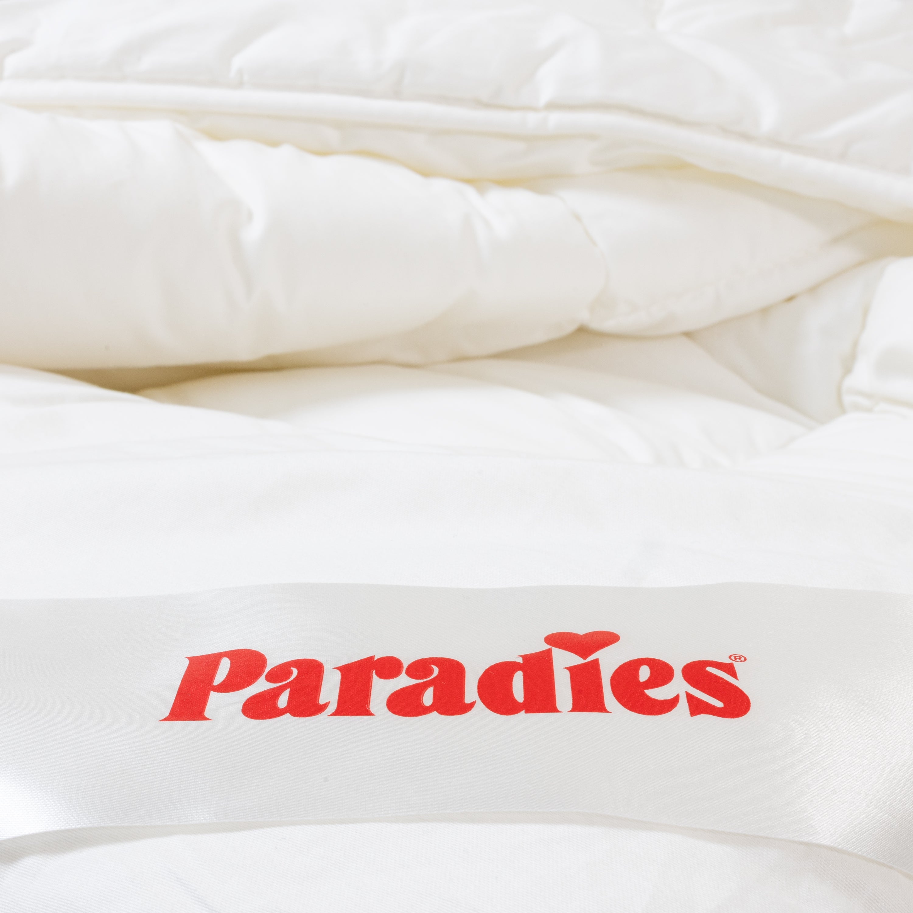 Detailaufnahme der gefalteten Ganzjahresdecke Avera Bio mit rotem Paradies-Logo auf dem Etikett