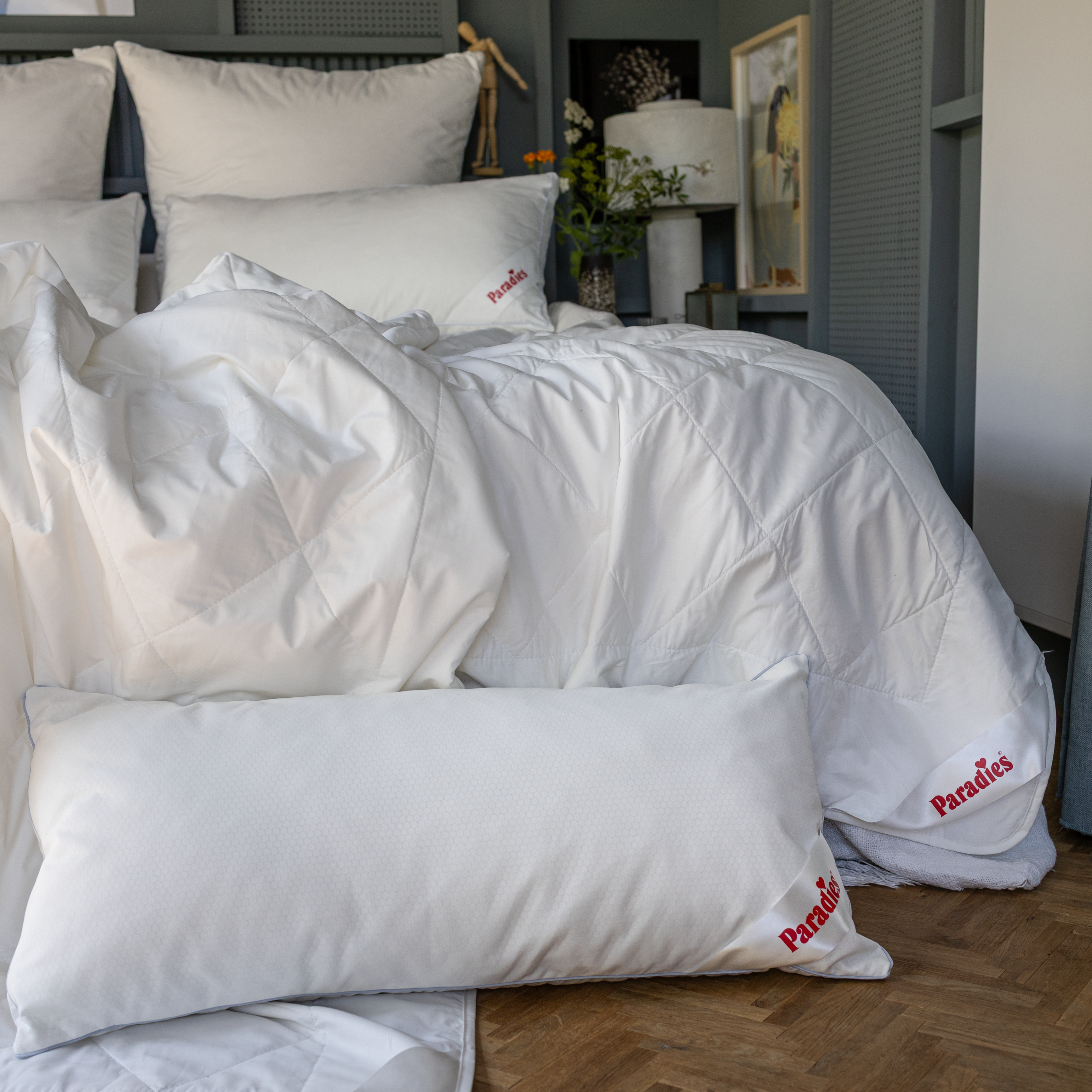 Weißes Bett mit Paradies Cool-Decke und mehreren Kissen, alle mit rotem Schriftzug 
