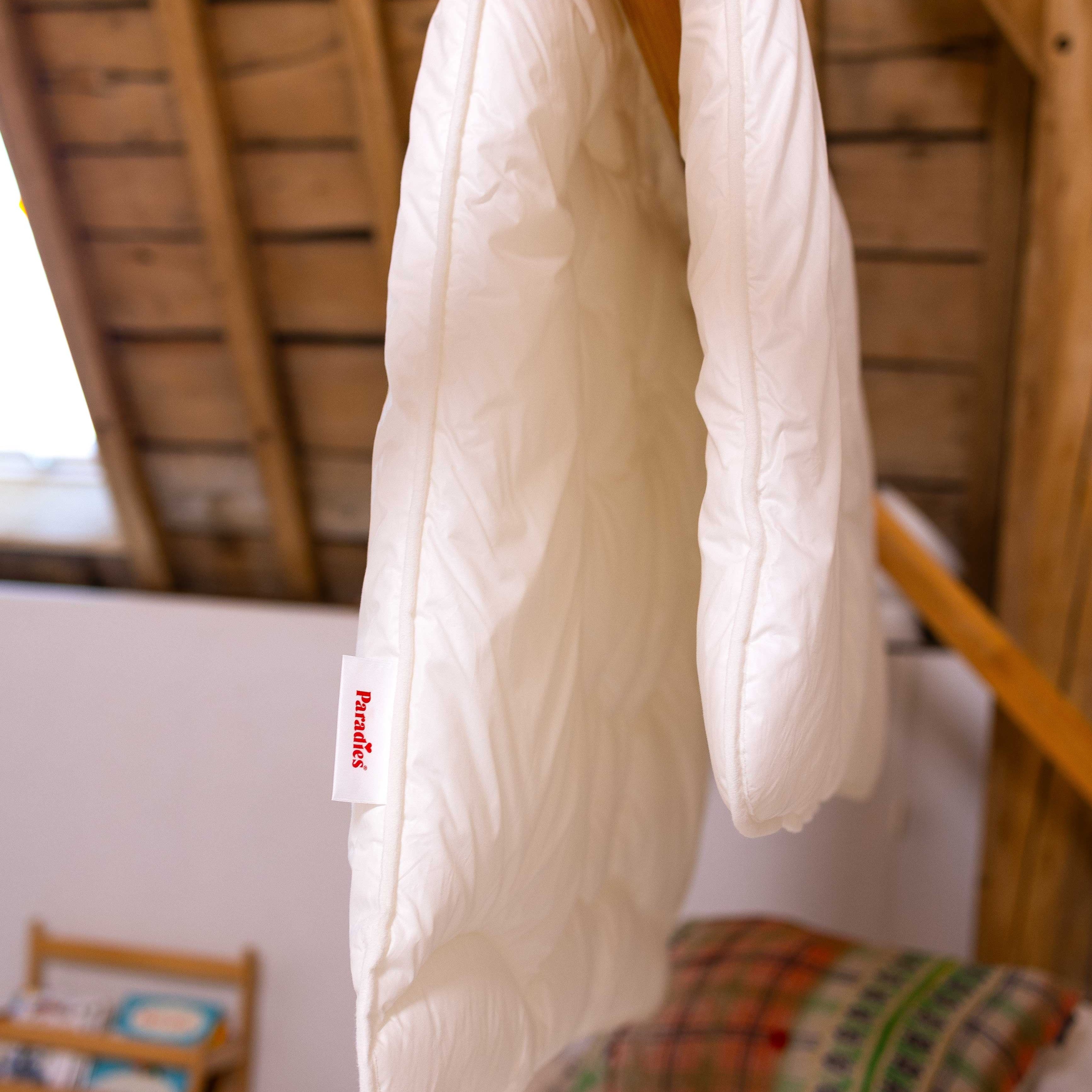 Weiße Kinderdecke Lova mit rotem Etikett 'Paradies' hängt über einem Holzbalken in einem Raum mit sichtbarer Holzbalkendecke