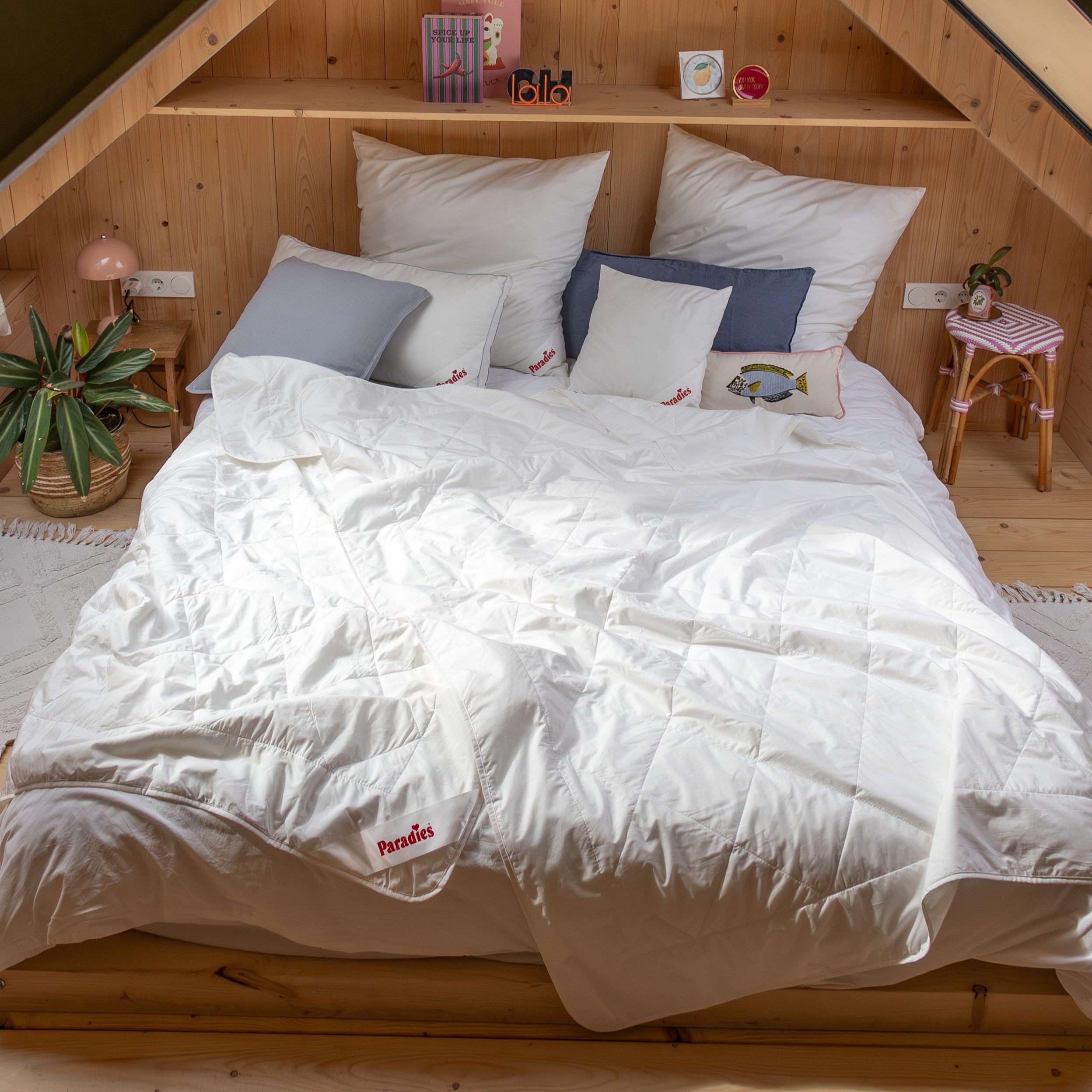 Holzbettrahmen mit weißen Bettdecken und mehreren Kissen vor einer schrägen Holzpaneelwand