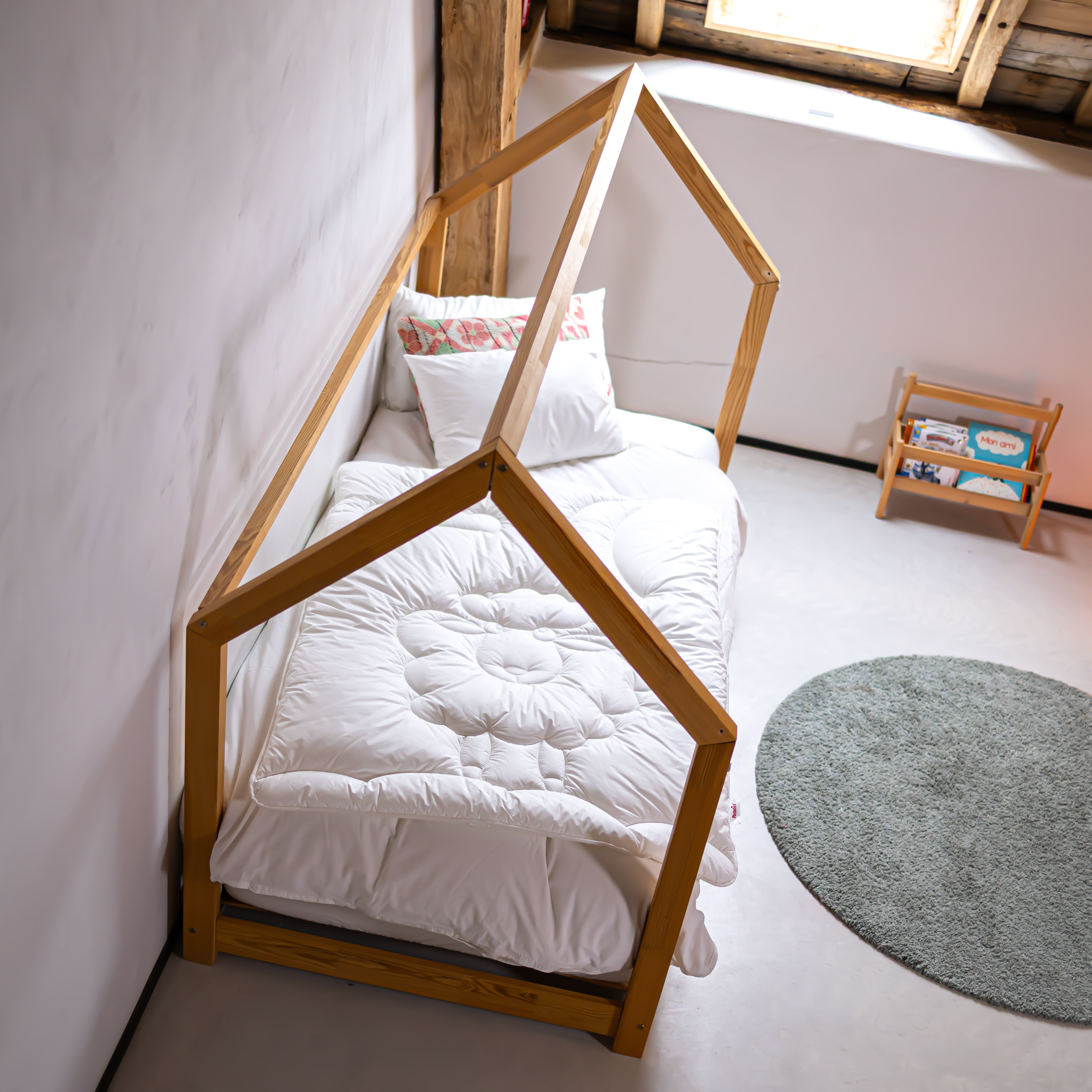 Kinderbett mit Holzrahmen in Hausform und weißer Steppbettdecke mit floralem Muster
