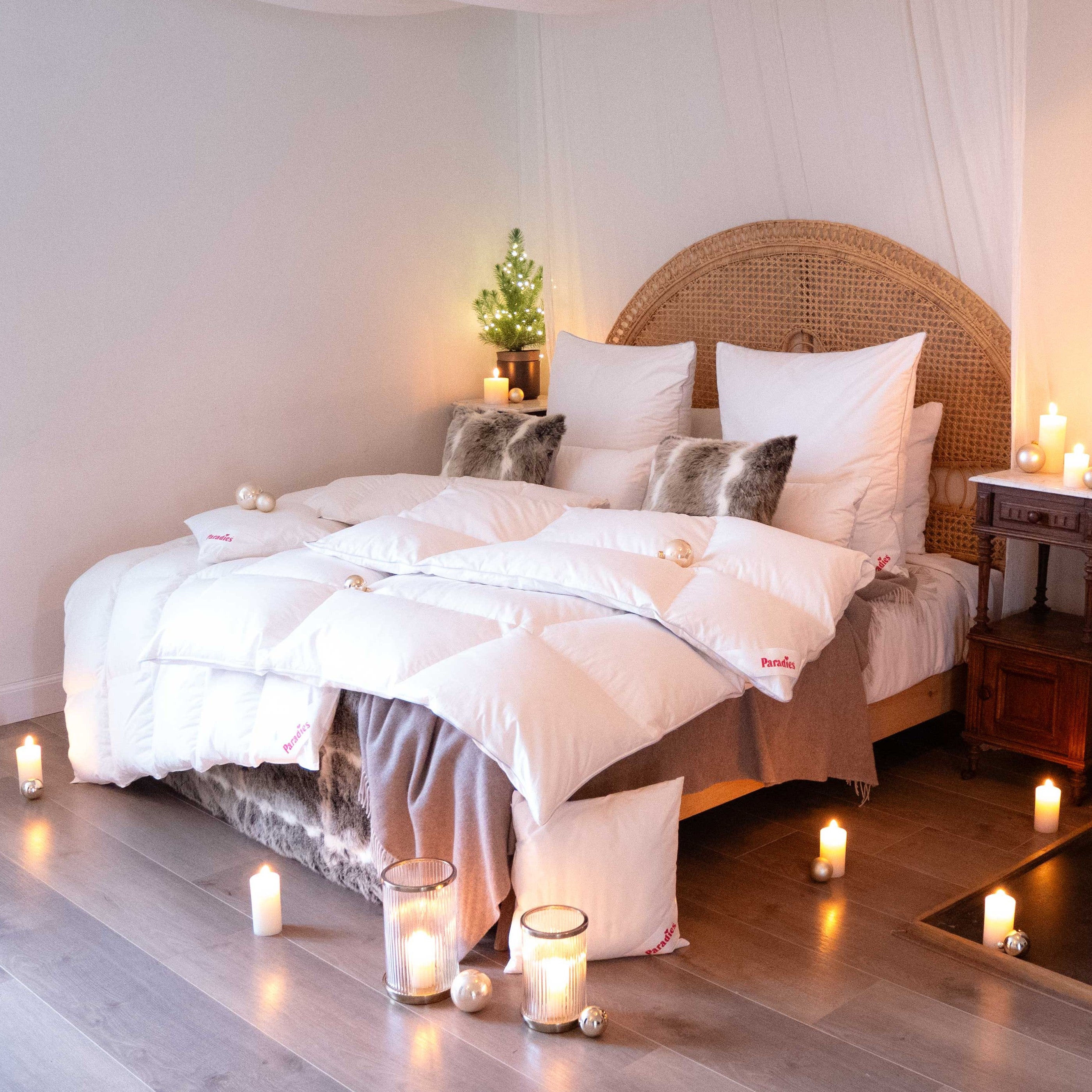 Gemütliches Schlafzimmer mit einem Bett, das mit einer weißen Daunendecke und grauen Kissen dekoriert ist, umgeben von brennenden Kerzen