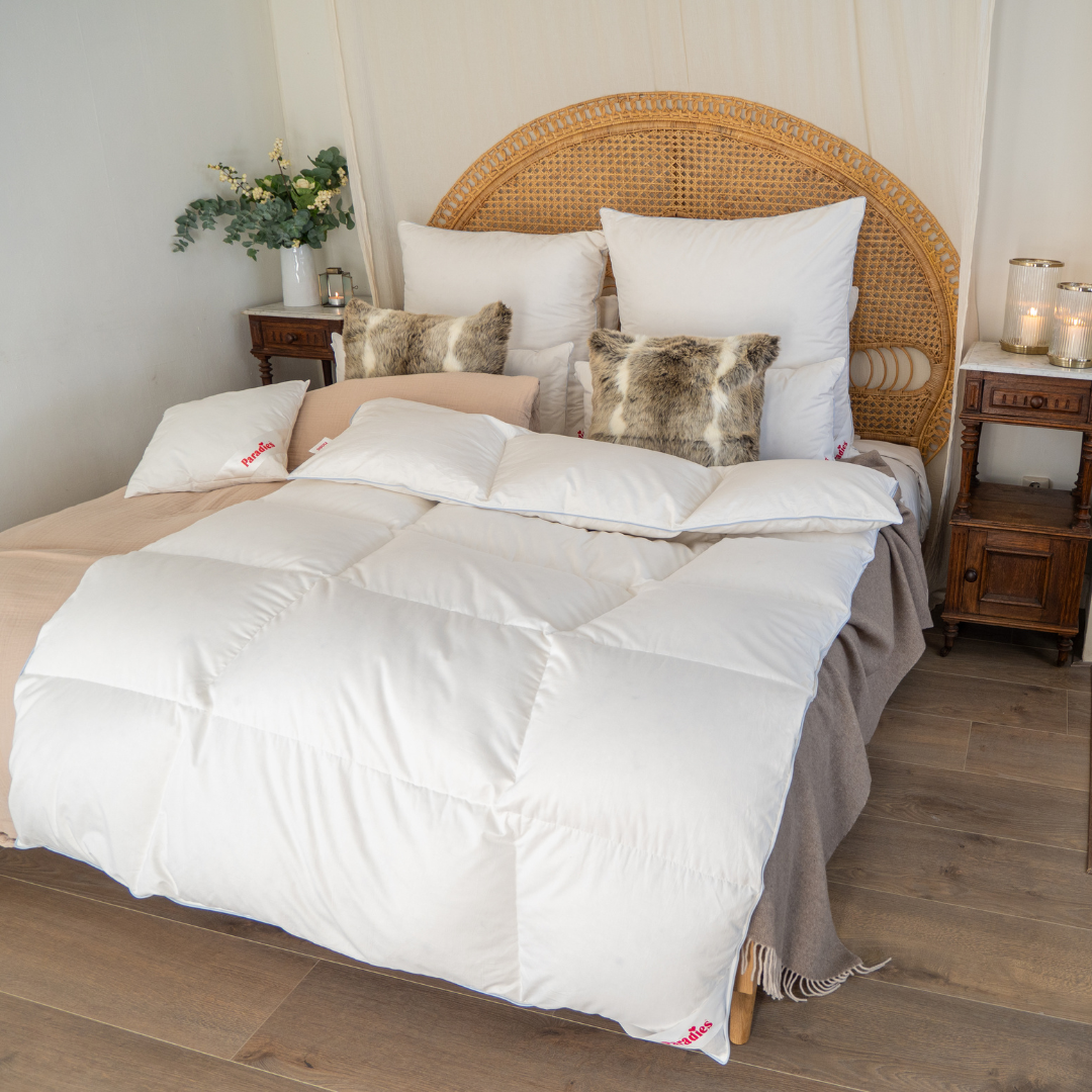 Winterbettdecke mit reiner Gänsedaunenfüllung auf einem Bett mit Rattankopfteil, dekoriert mit weißen und Fellkissen
